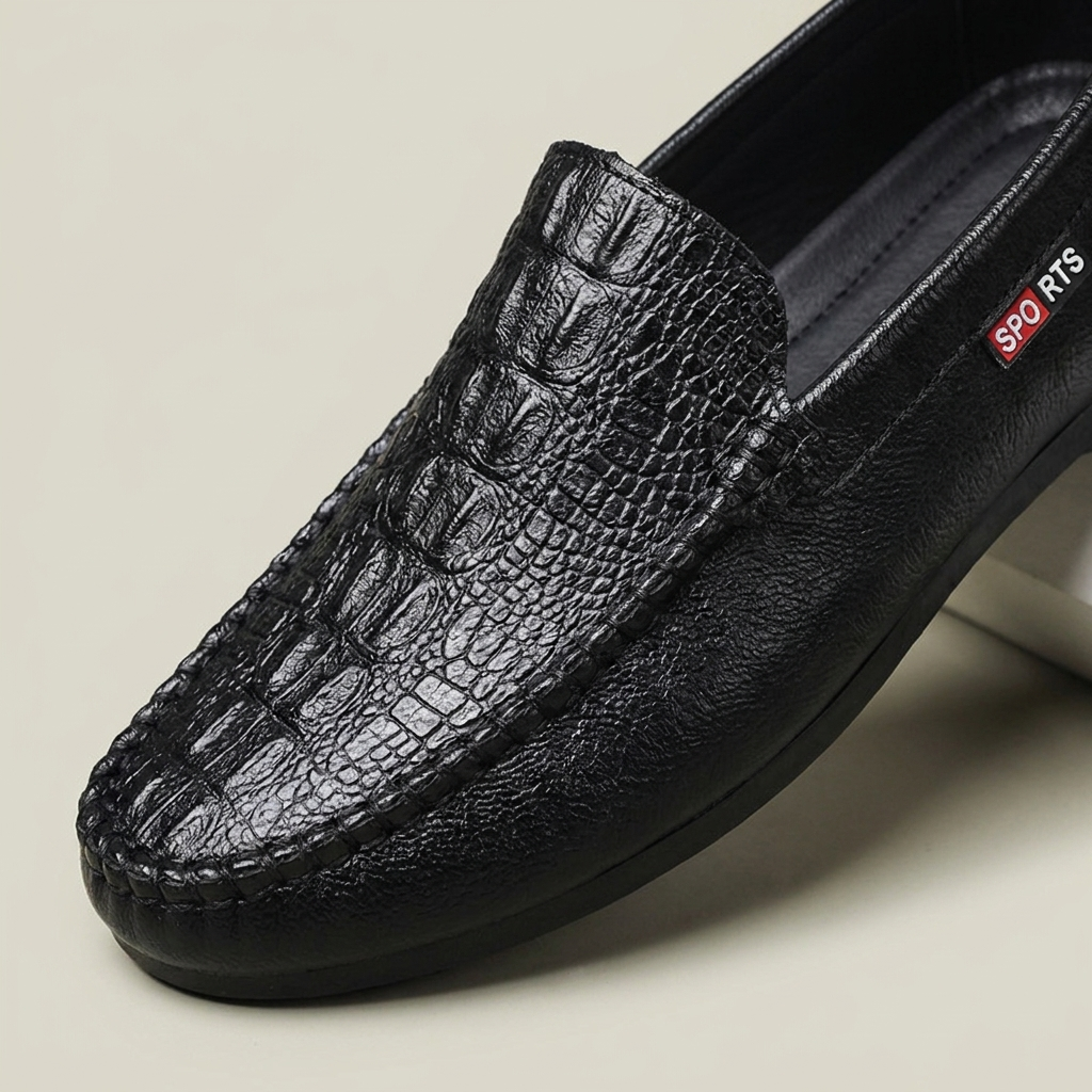 Front detail close-up of black synthetic leather crocodile-grain slip-on loafer showing round toe, stitch detail, and PU insole